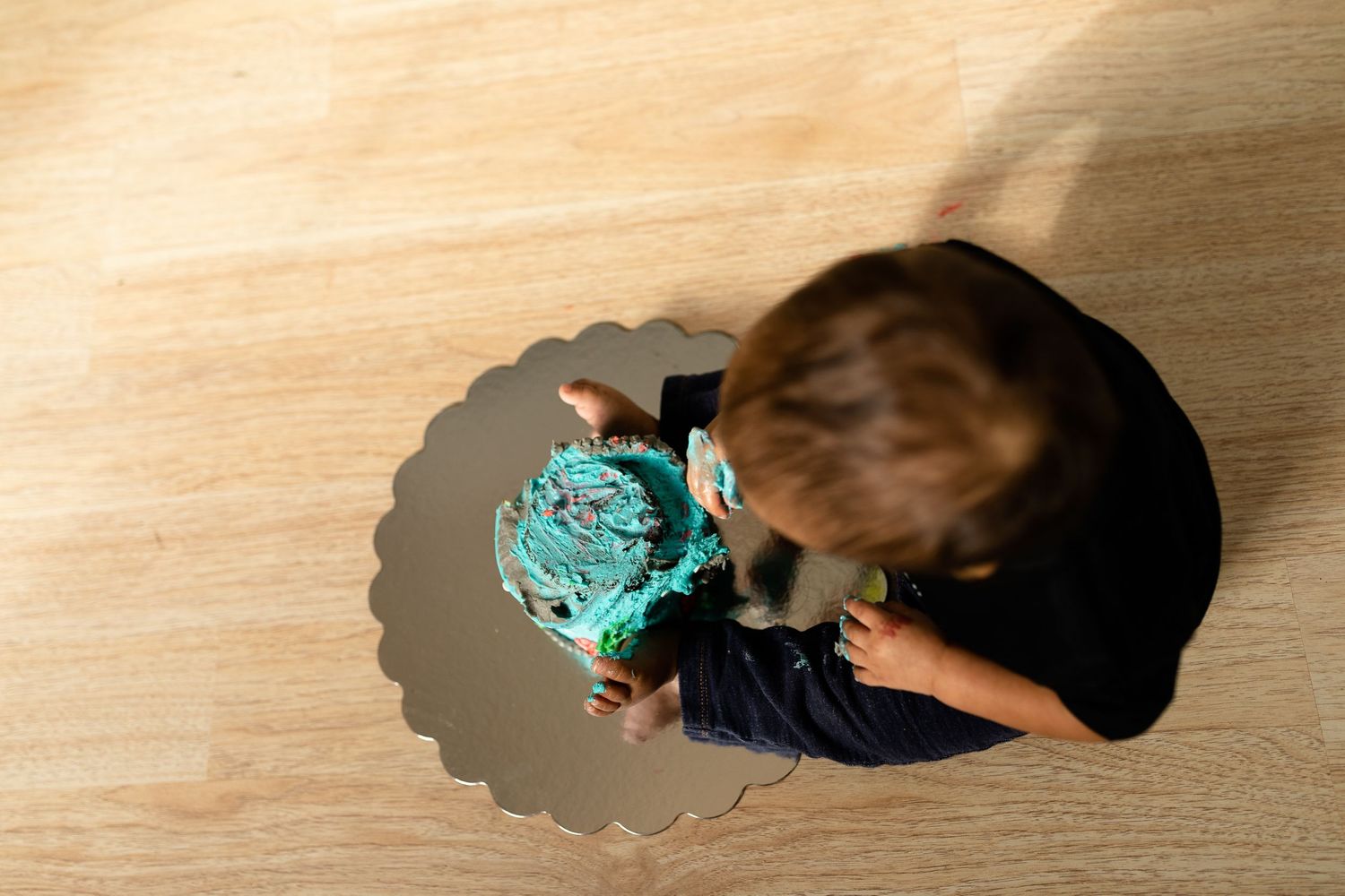 Aerial view of children playing with turquoise toy on light hardwood floor.