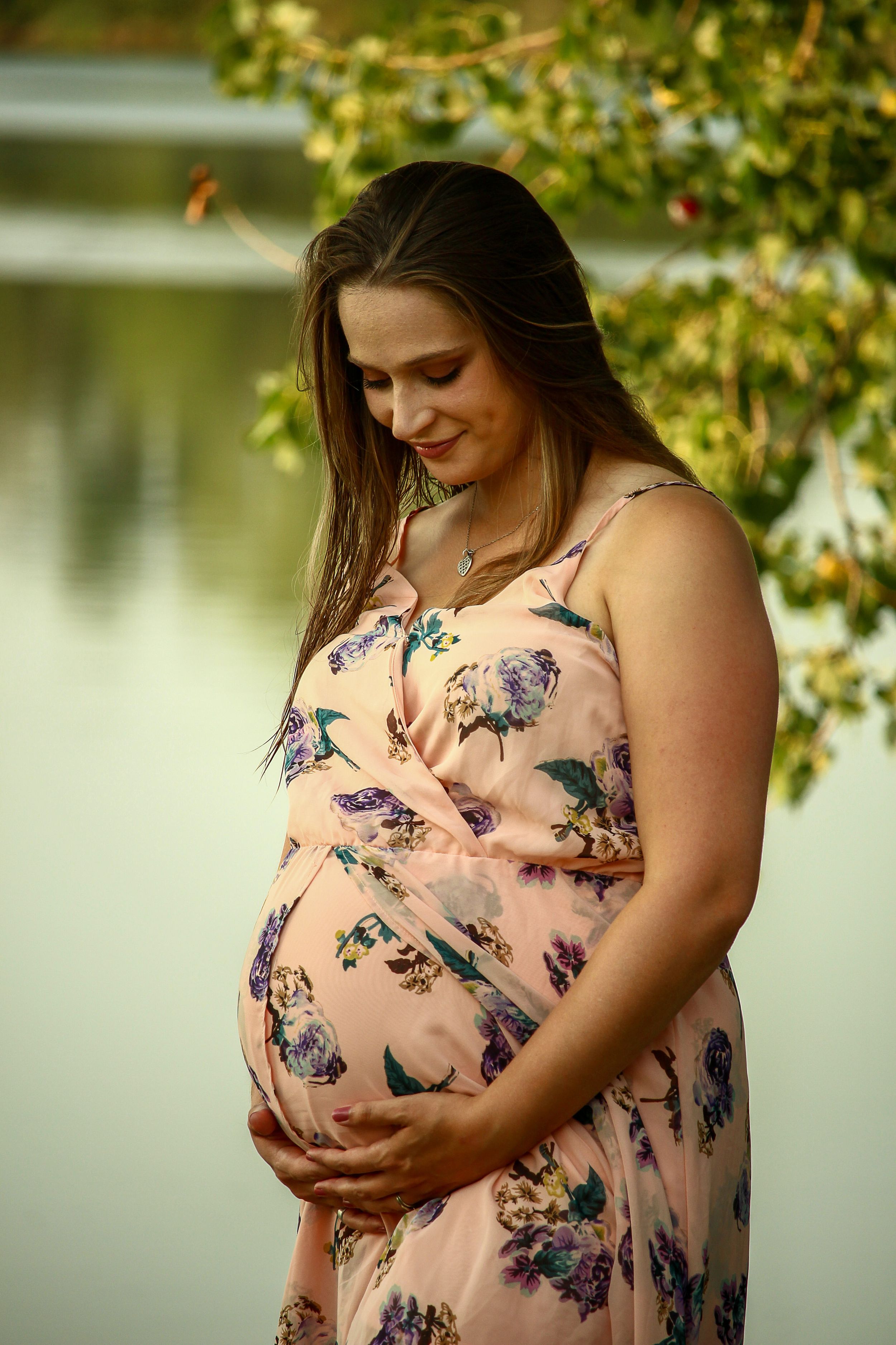 Maternity photoshoot in a peach floral dress by a peaceful lake during golden hour.