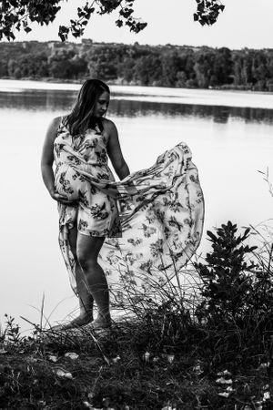 A floral dress flows in the breeze by a serene lakeside during a black and white photoshoot.