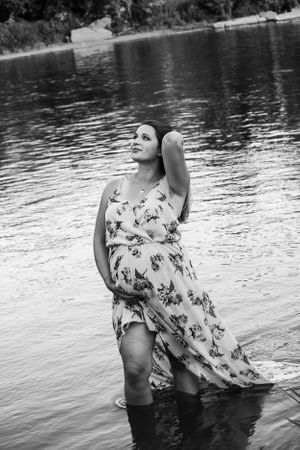 Person in a flowing floral dress stands knee-deep in calm lake waters at sunset.