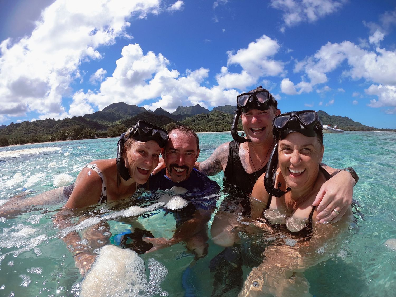 Four snorkelers pose together in tropical turquoise waters with mountains in background.