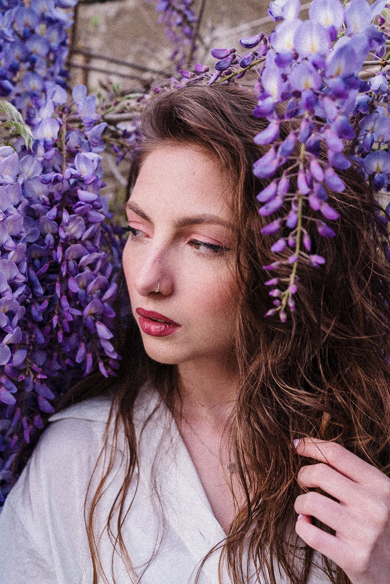 Portrait among blooming purple wisteria flowers with soft natural lighting.