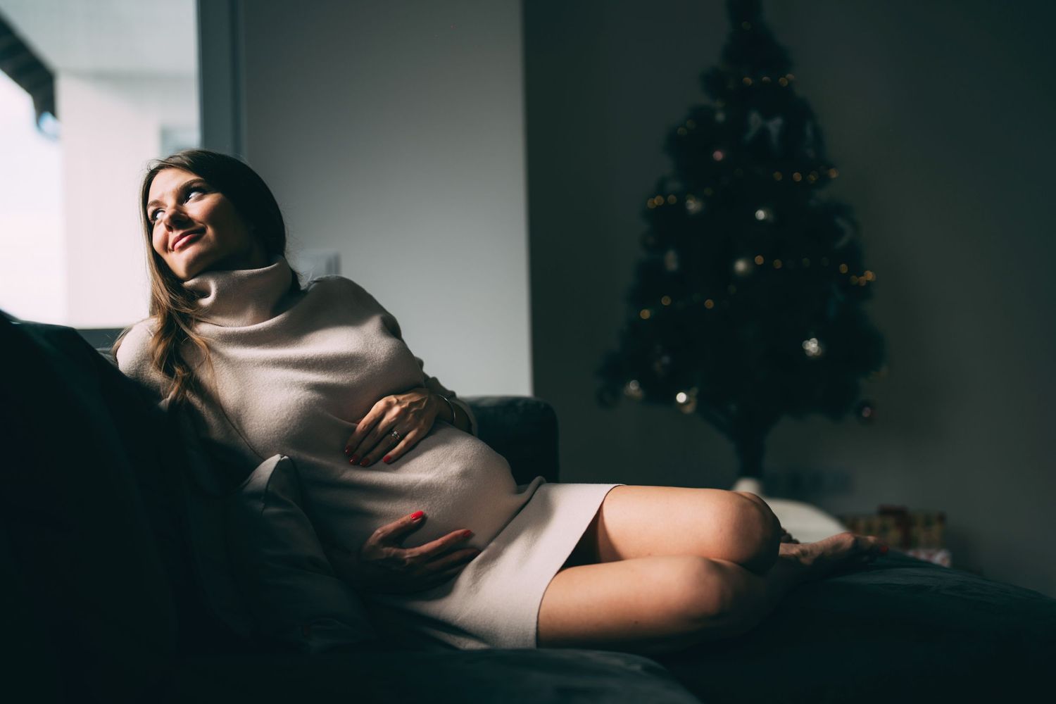 Moody holiday portrait of person lounging on couch near Christmas tree.