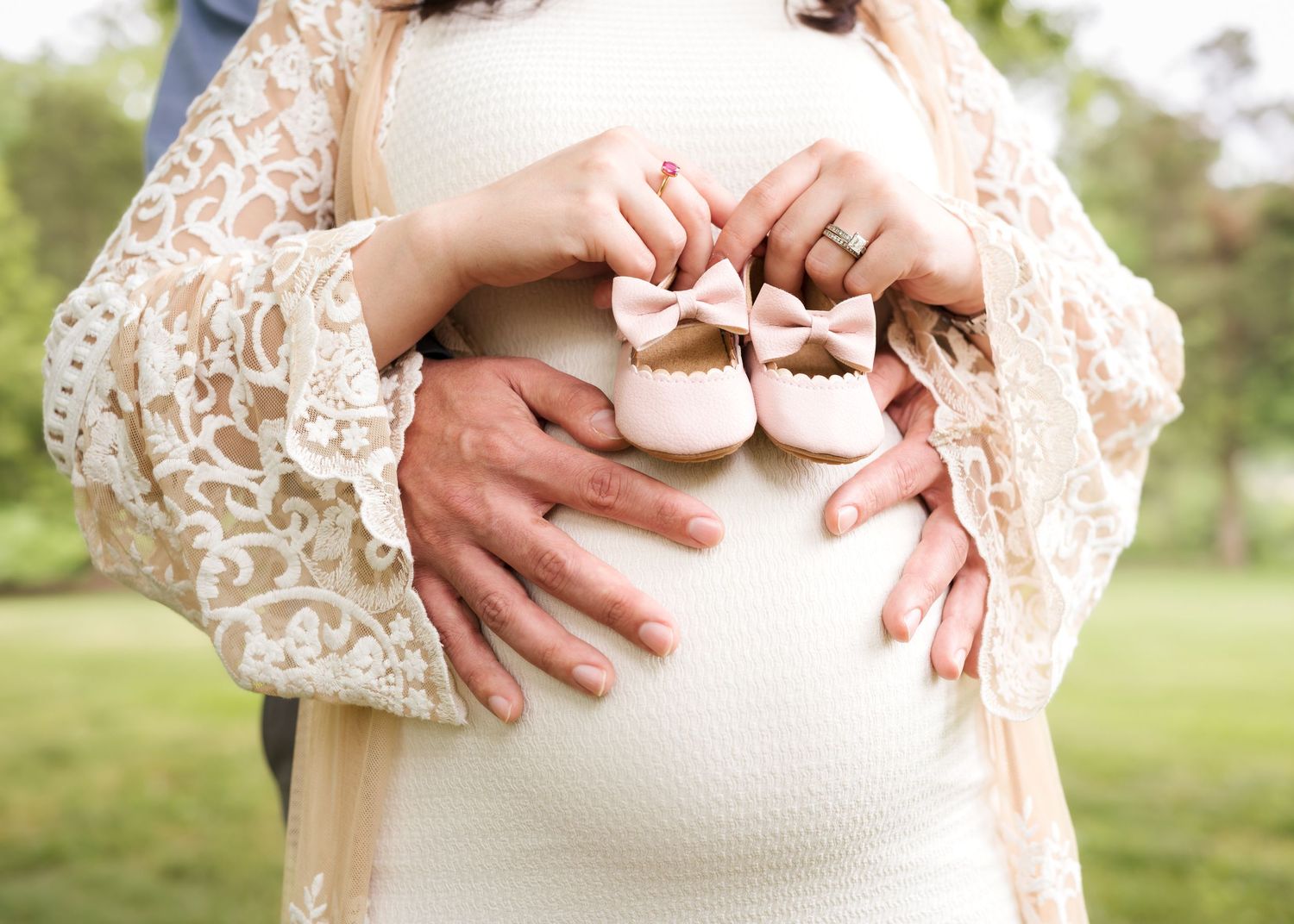 Close up of hands holding tiny baby shoes against a pregnant belly in lace.