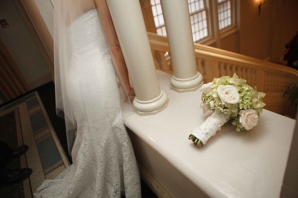 Wedding dress train and bouquet of white roses cascade elegantly down a sunlit marble staircase.