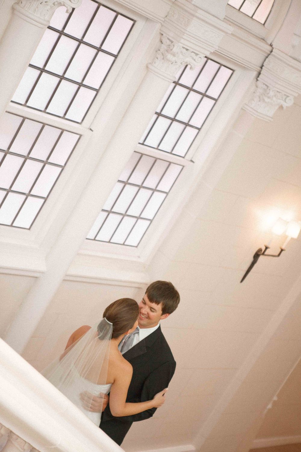 Romantic wedding scene with a couple sharing a loving dance under high windows in a bright white studio space.