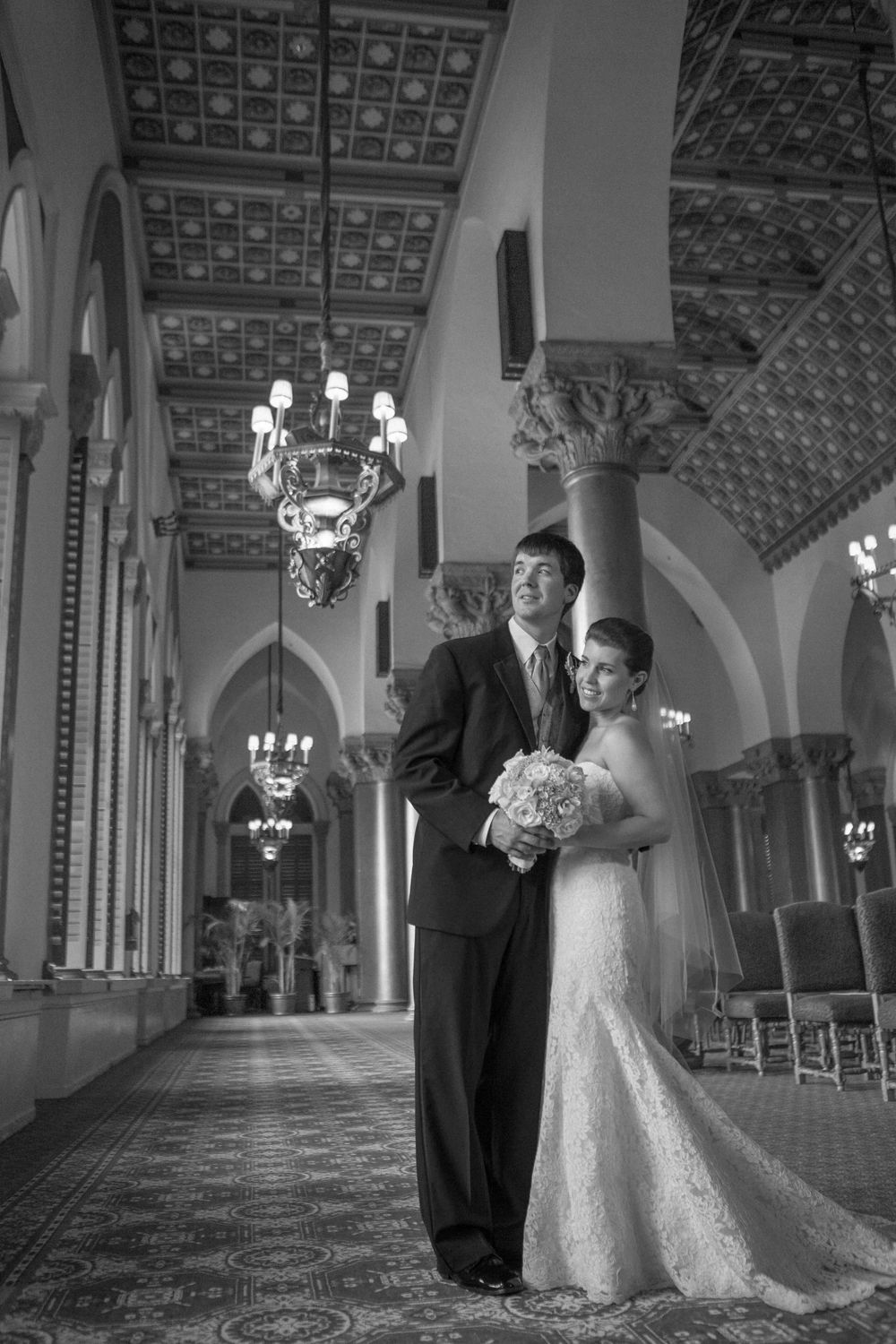 Black and white wedding photographs showing a couple posing in an elegant ballroom with ornate architecture and chandeliers.