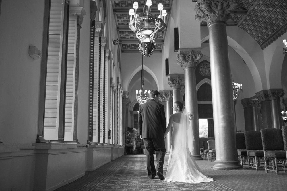 Elegant black and white wedding photo series showing a bride and groom in a grand church hallway with arches and columns.