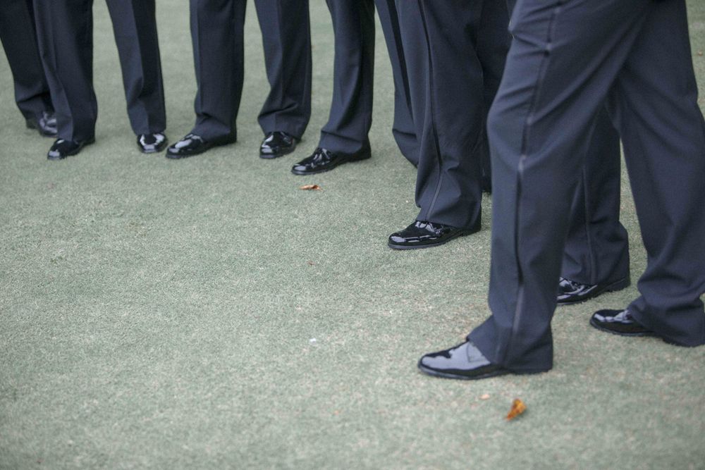 Business professionals in dark suits stand in a group on concrete ground with a small orange ball visible near their feet.