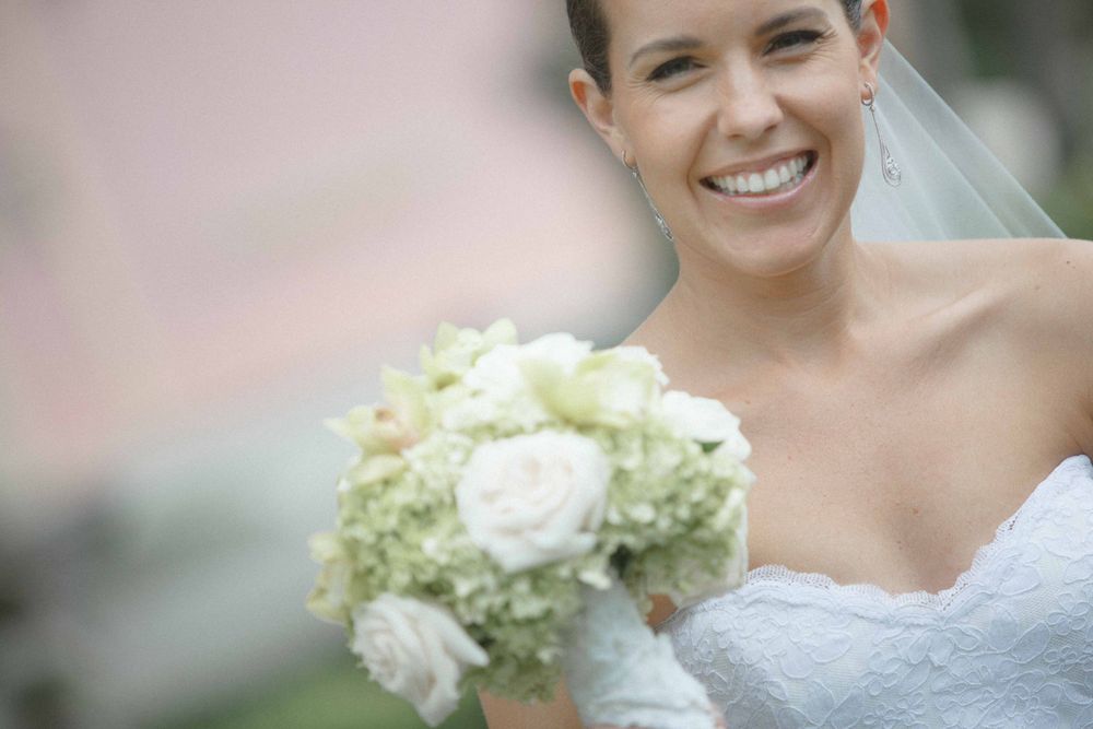 A radiant bride in a white strapless gown holds a beautiful bouquet of white roses and green hydrangeas.