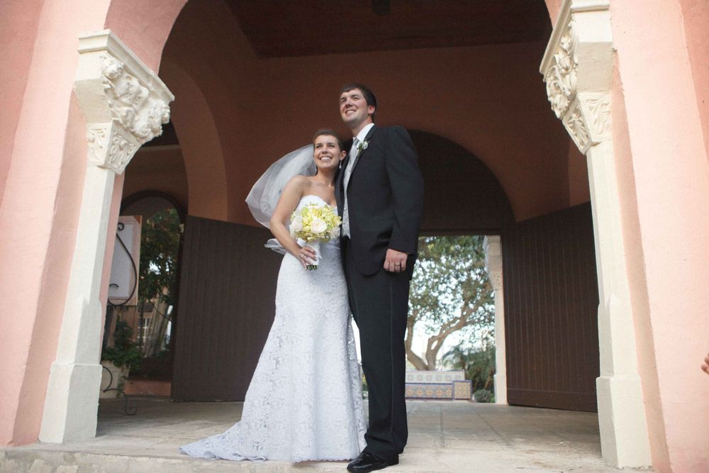 A married couple poses under elegant pink archways at a Mediterranean-style wedding venue.