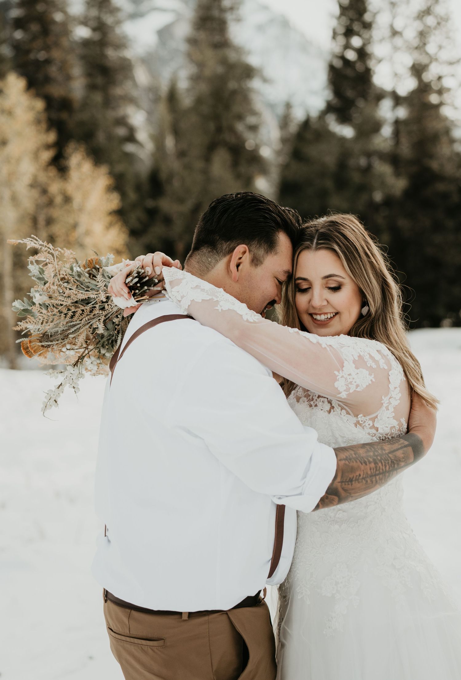 Romantic winter wedding portrait with couple embracing among snowy pine trees.