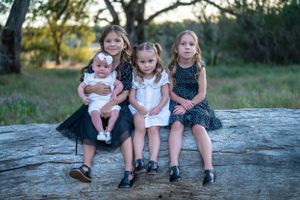 Children sitting together on a large rock in a wooded outdoor setting during golden hour.