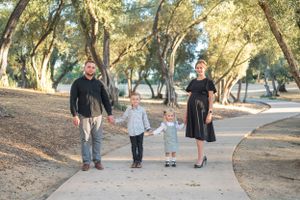 A family walks together on a tree-lined path during golden hour in a park setting.