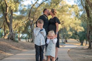 Family members share a playful moment on a winding path surrounded by trees.