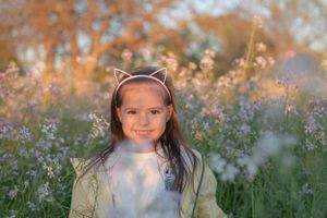 Young child wearing cat ears headband smiles in a field of spring flowers.