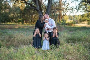 Family portrait taken outdoors in a natural grassy field with trees in golden evening light.