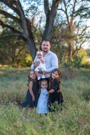 Sweet family portrait with young children gathered under a large tree at sunset.