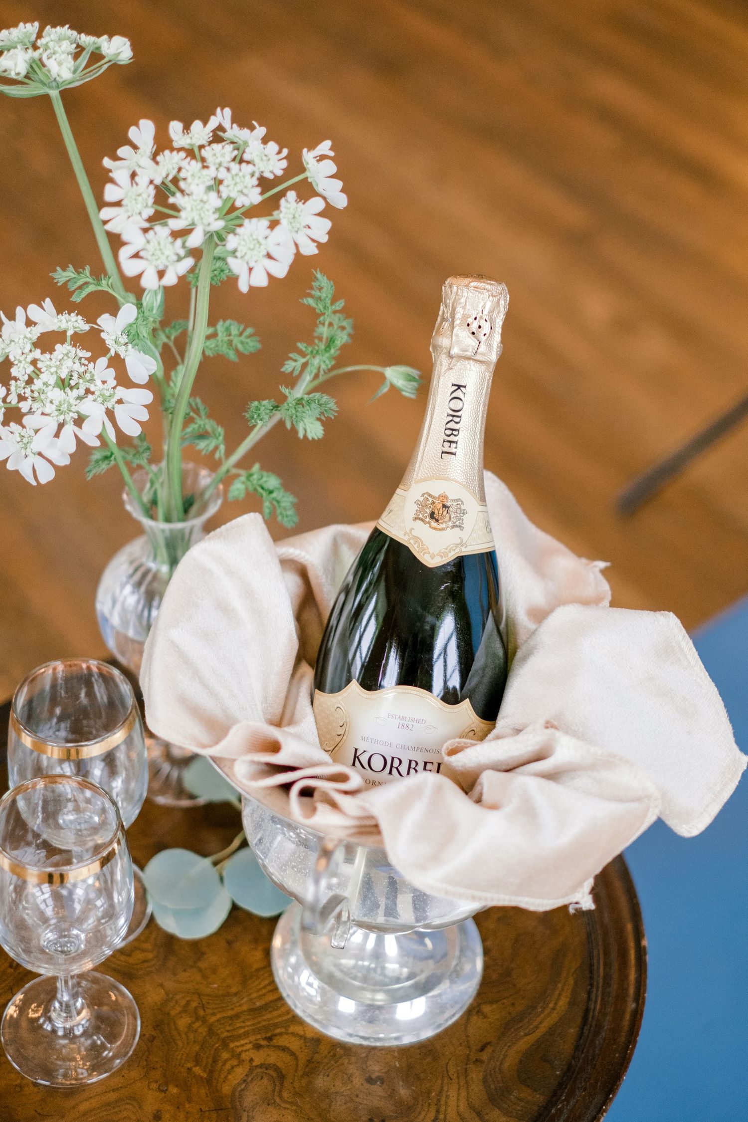 Elegant display of Korbel champagne with delicate white flowers and crystal glasses on wooden table.