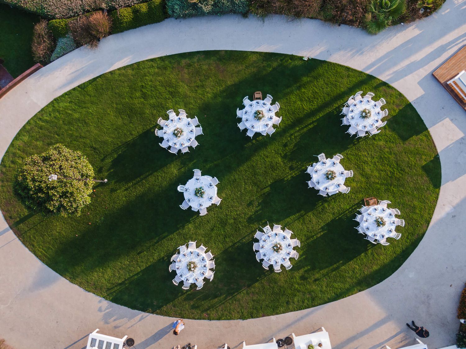 Aerial view of white circular umbrella tables arranged in a snowflake pattern on a manicured lawn surrounded by walkways.