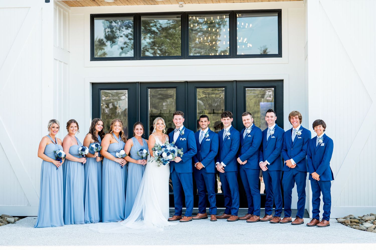 Wedding party wearing light blue dresses and navy suits pose together for group photos.