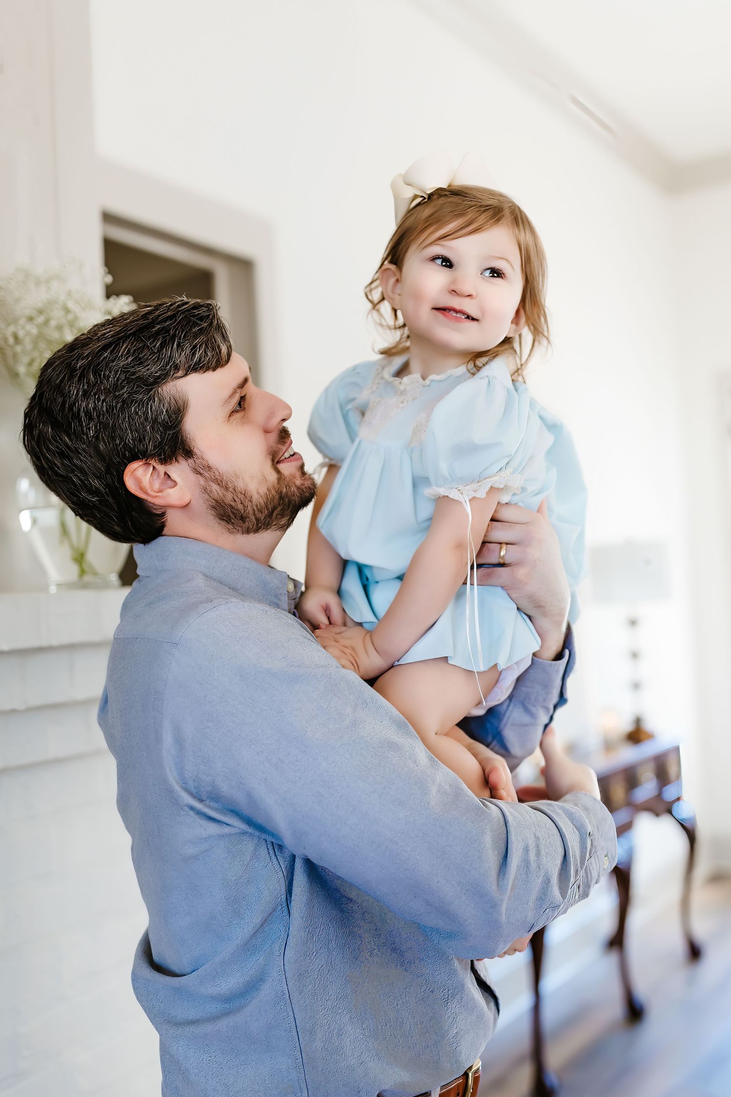 Parent holding child in light-filled room with white interior decor.