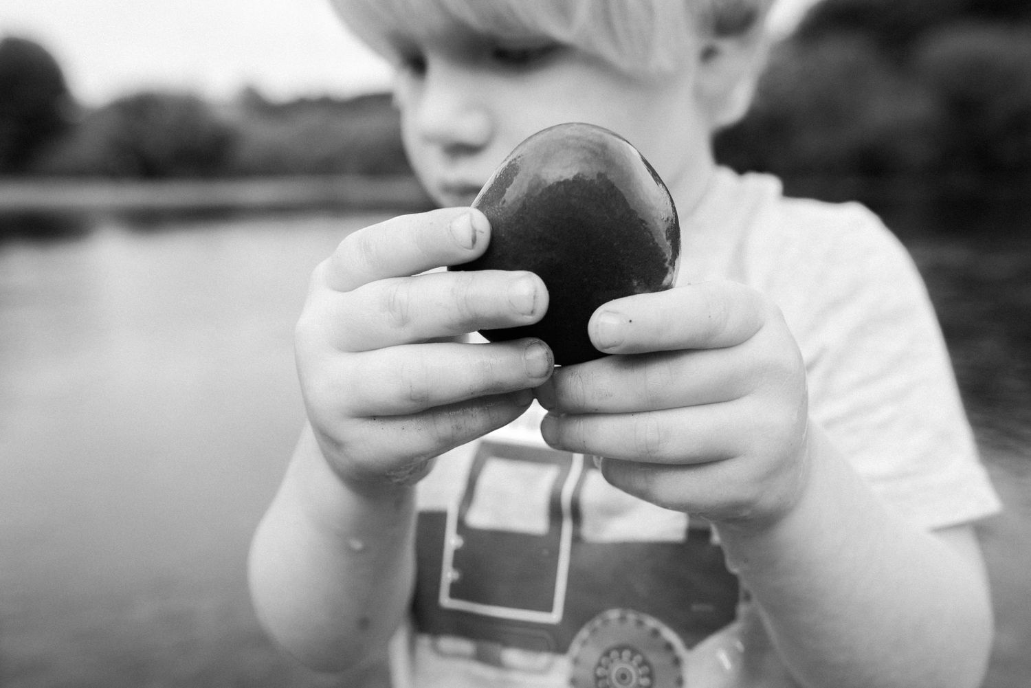 black and white photo of Theo holding up a stone to the camera that he found in the river.
