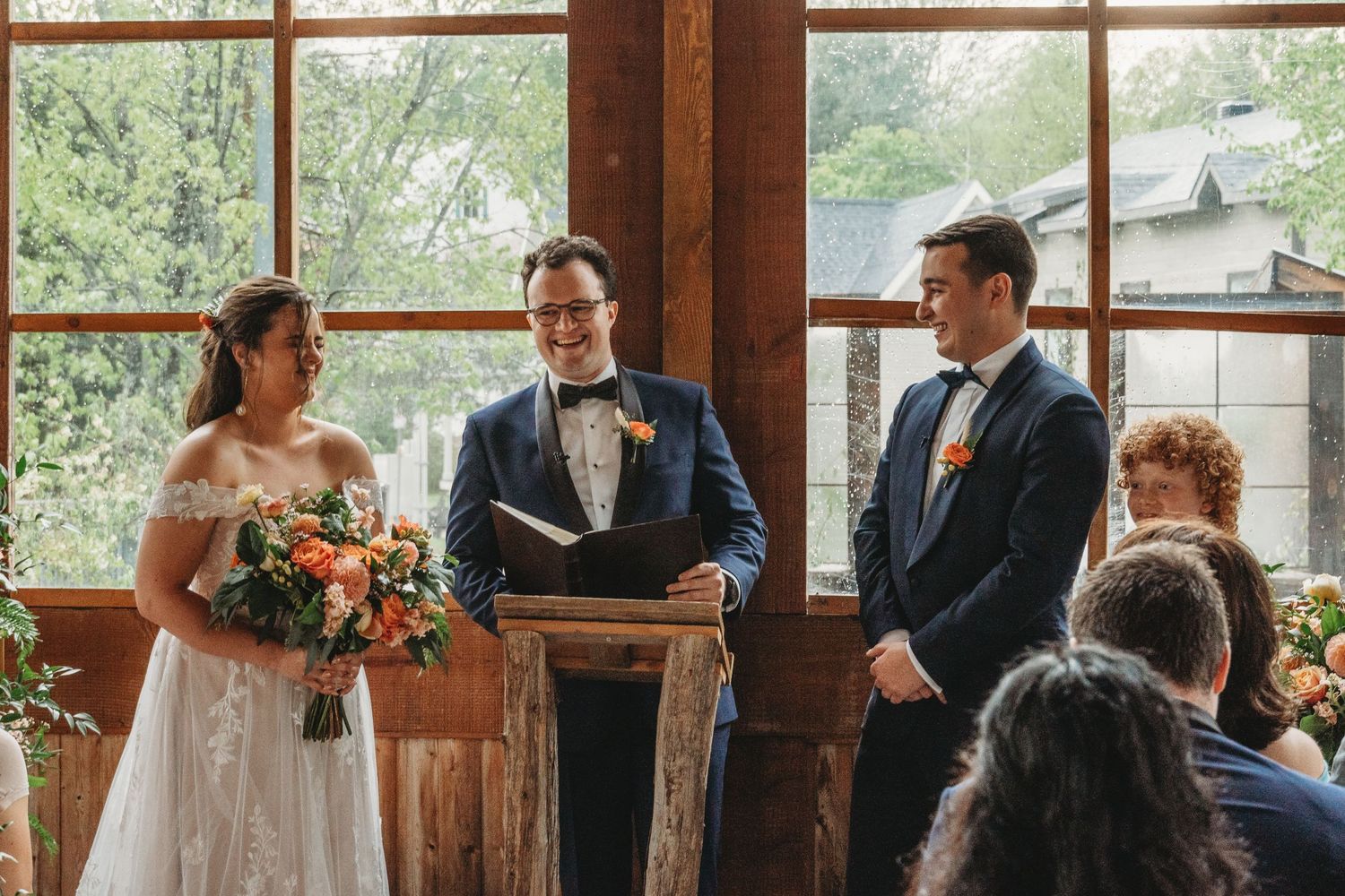 Indoor wedding ceremony with officiant and couple at rustic wooden venue with large windows.