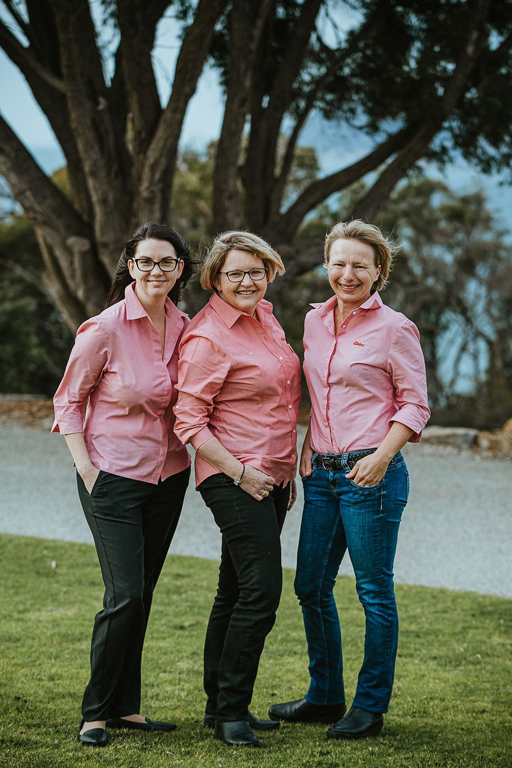 Three people in matching pink button-down shirts pose together on green grass.