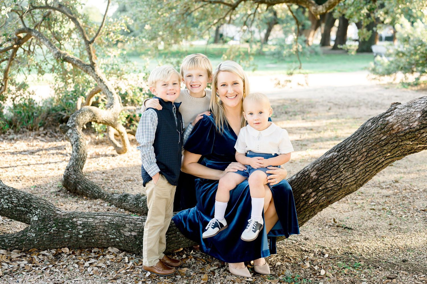 Family sitting together on tree branch in outdoor natural setting.
