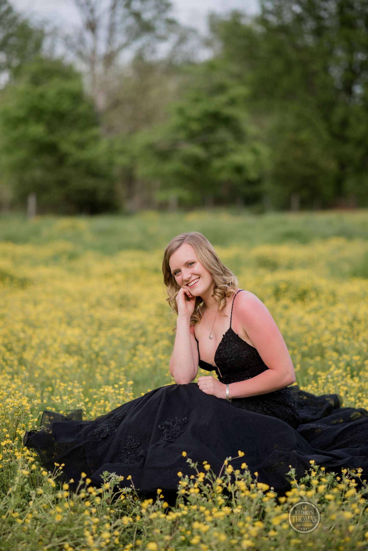 Woman in black formal dress poses gracefully in a field of yellow wildflowers during a golden hour photoshoot.