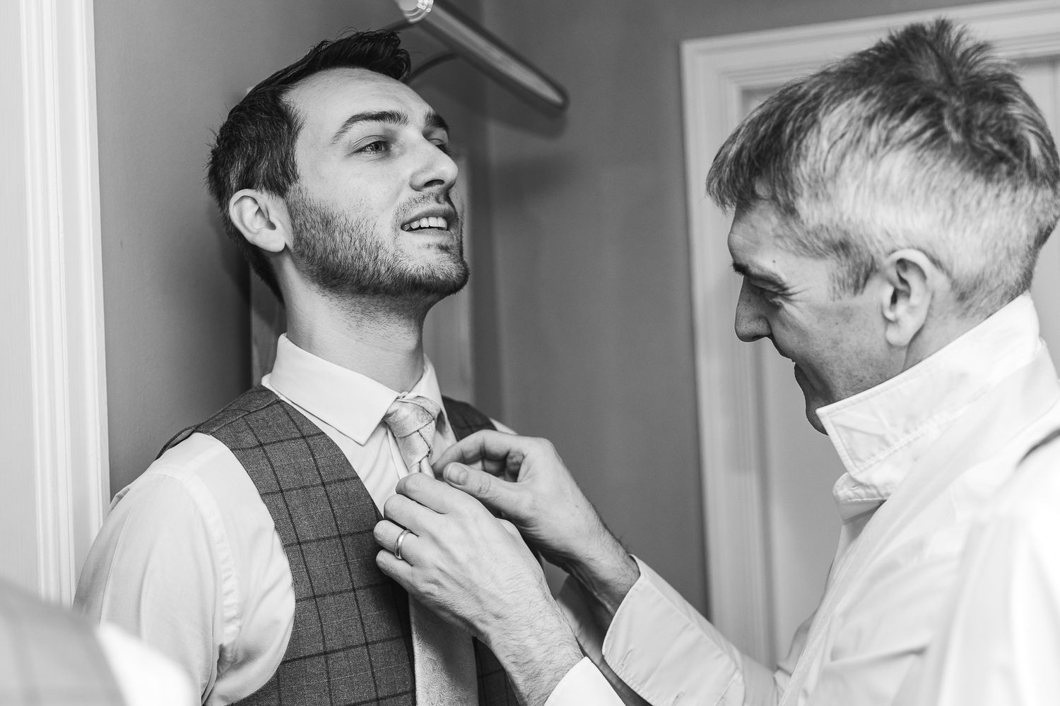 Black and white image showing final adjustments of groom's attire.