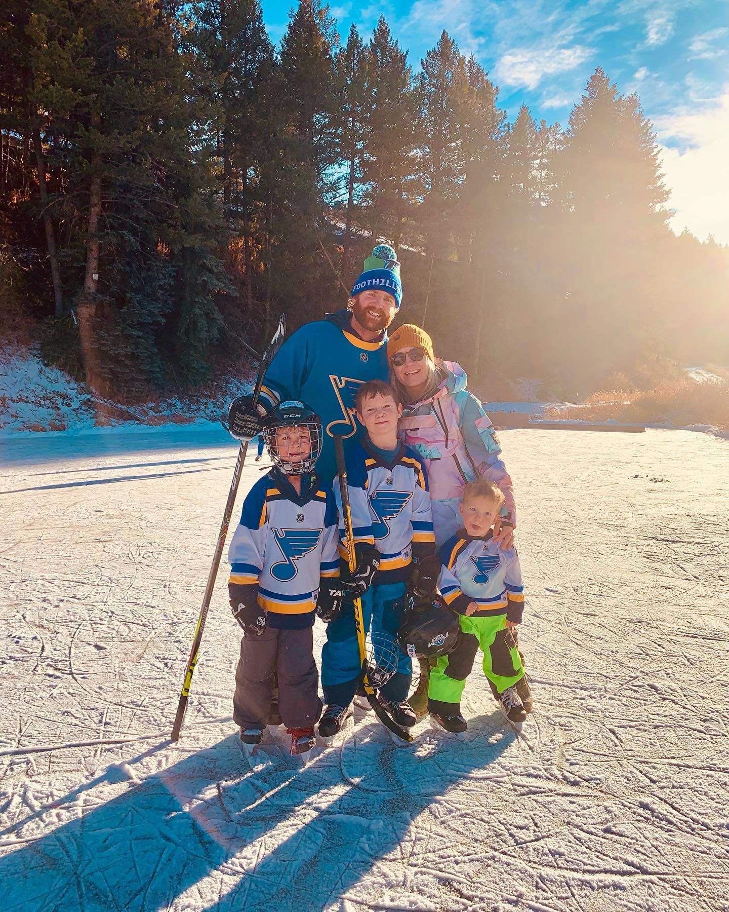A family poses together on snowy terrain while skiing on a bright winter day with evergreen trees in the background.
