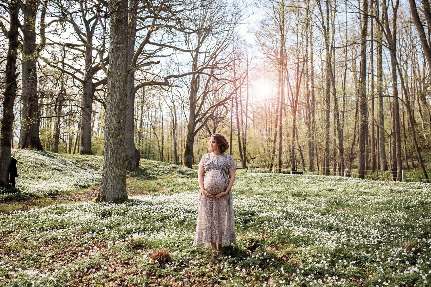 gravid kvinna står i en leopardmönstrad klänning i skogen och håller om den växande magen