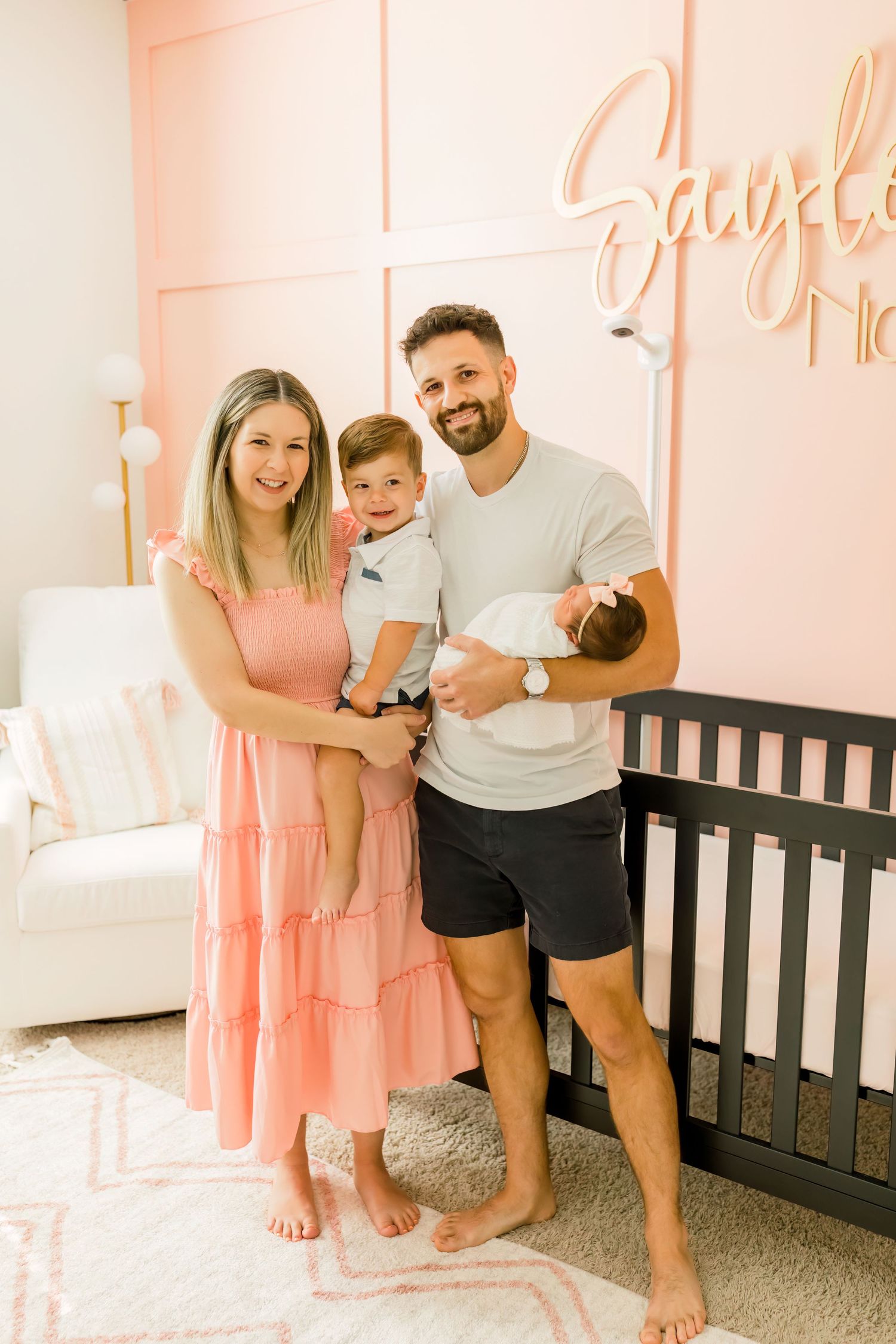 A family photo in a nursery with pink walls and black crib.
