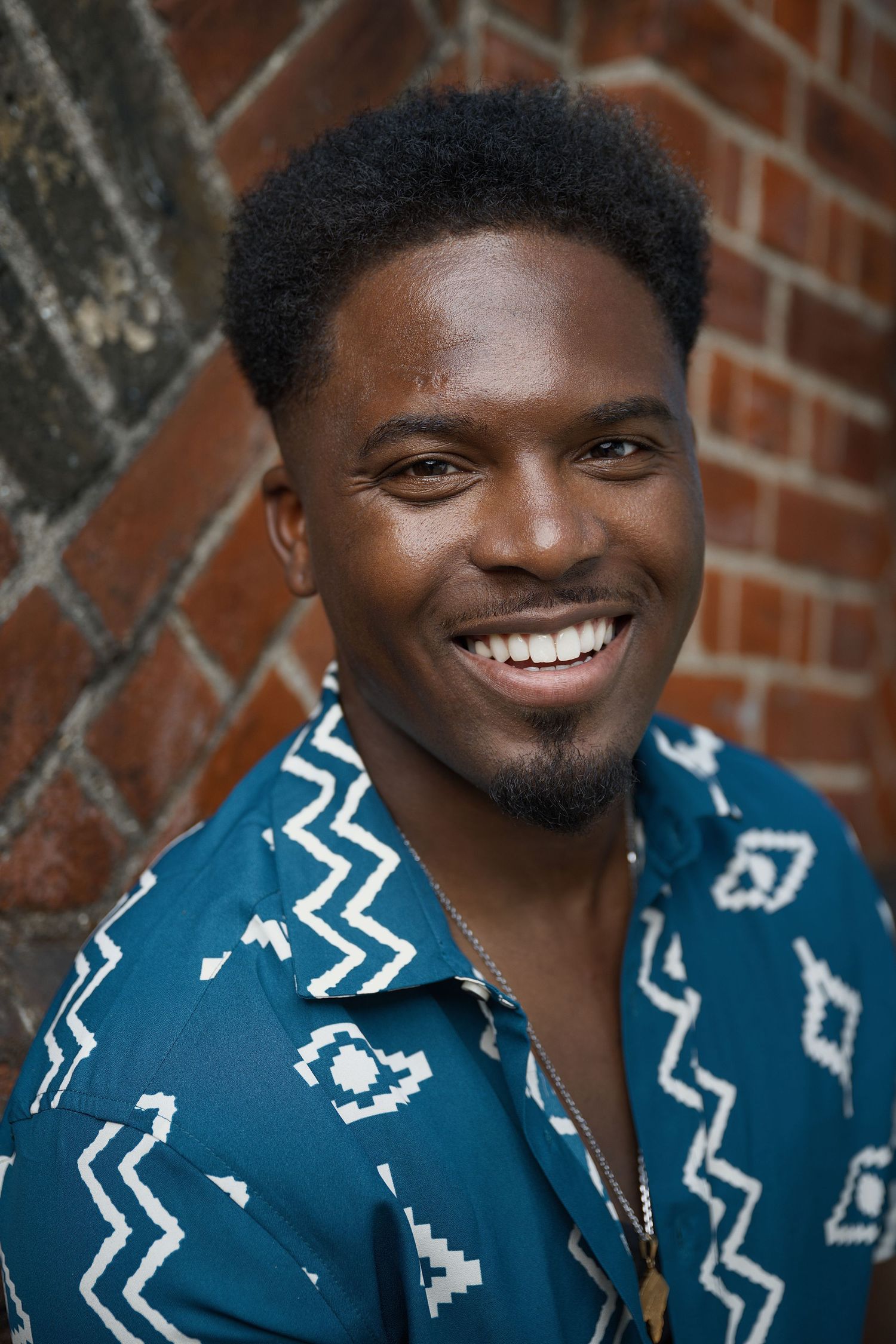 Portrait against brick wall wearing patterned blue shirt.