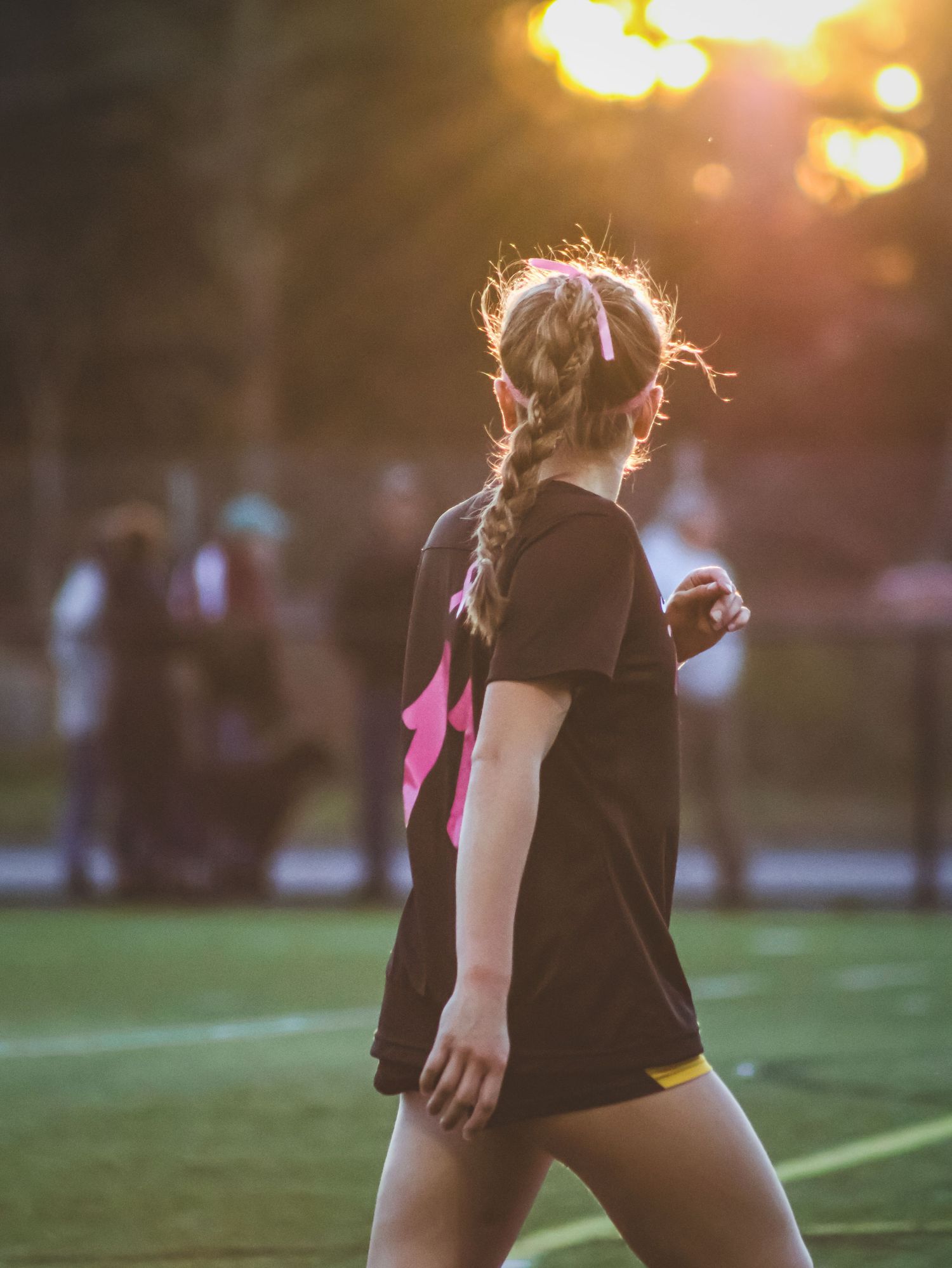 female soccer player walking on the field with the sun glowing behind her.