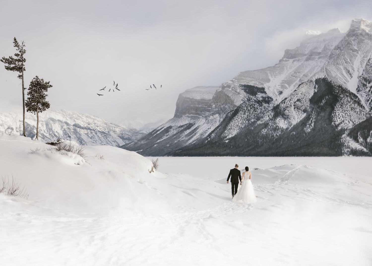 Snow-covered mountain landscape with distant figures walking across frozen Lake Louise.