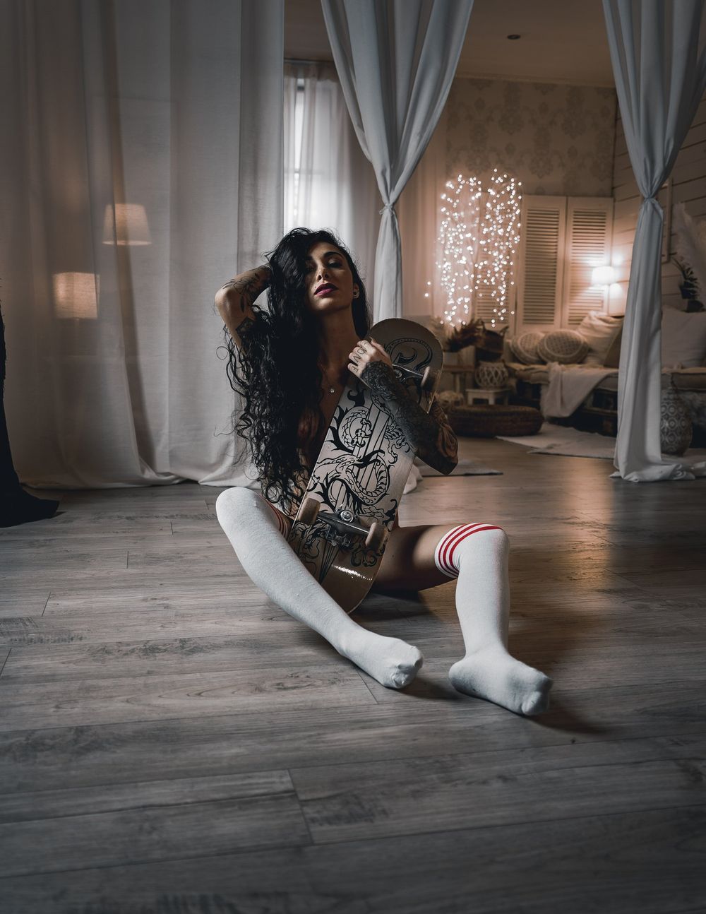 Indoor boudoir photo featuring skateboard and white knee-high socks on hardwood floor.