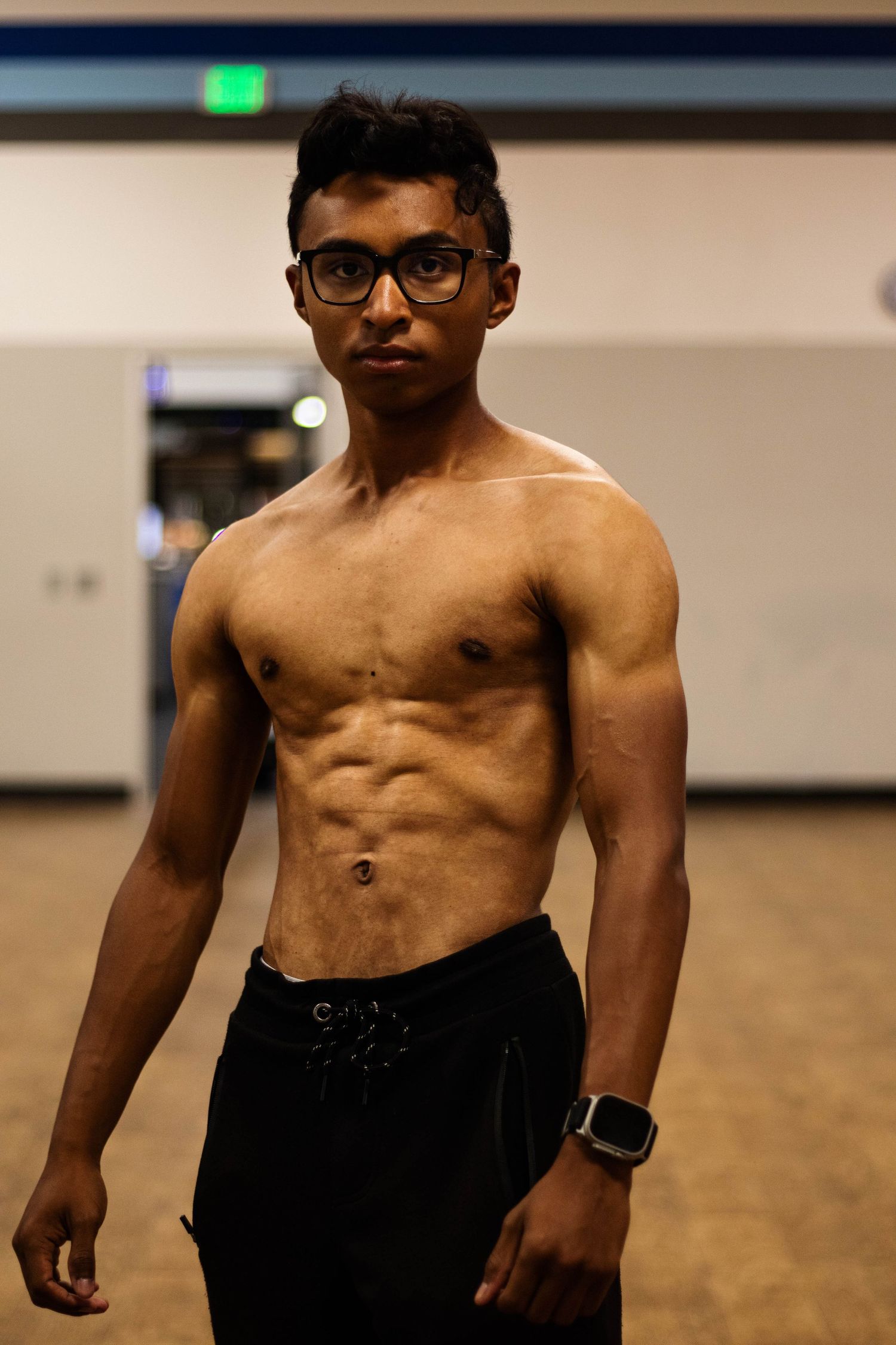Fitness model displaying muscular physique in indoor gym setting.
