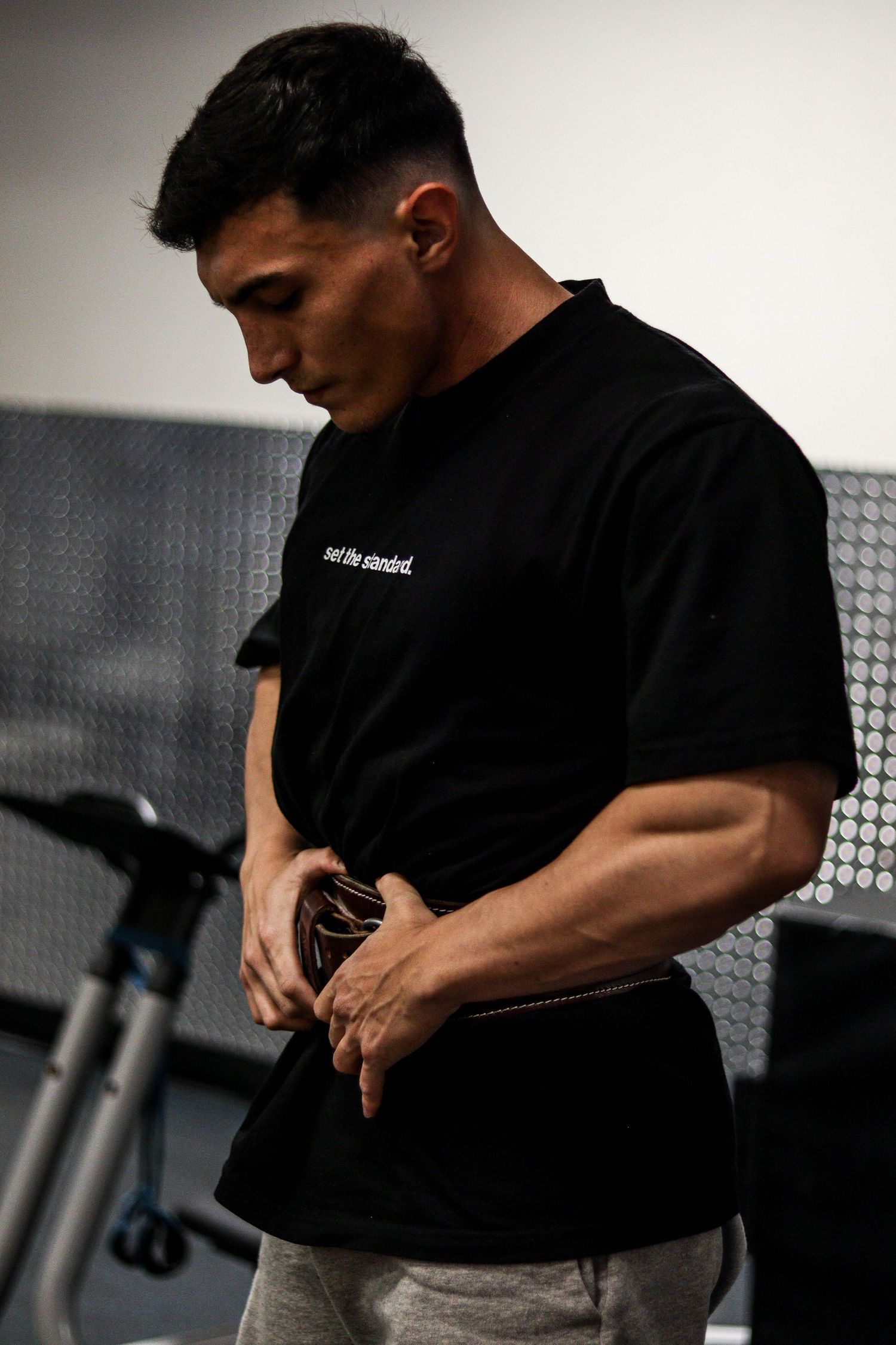 Athletic figure in black t-shirt and grey pants at fitness center.