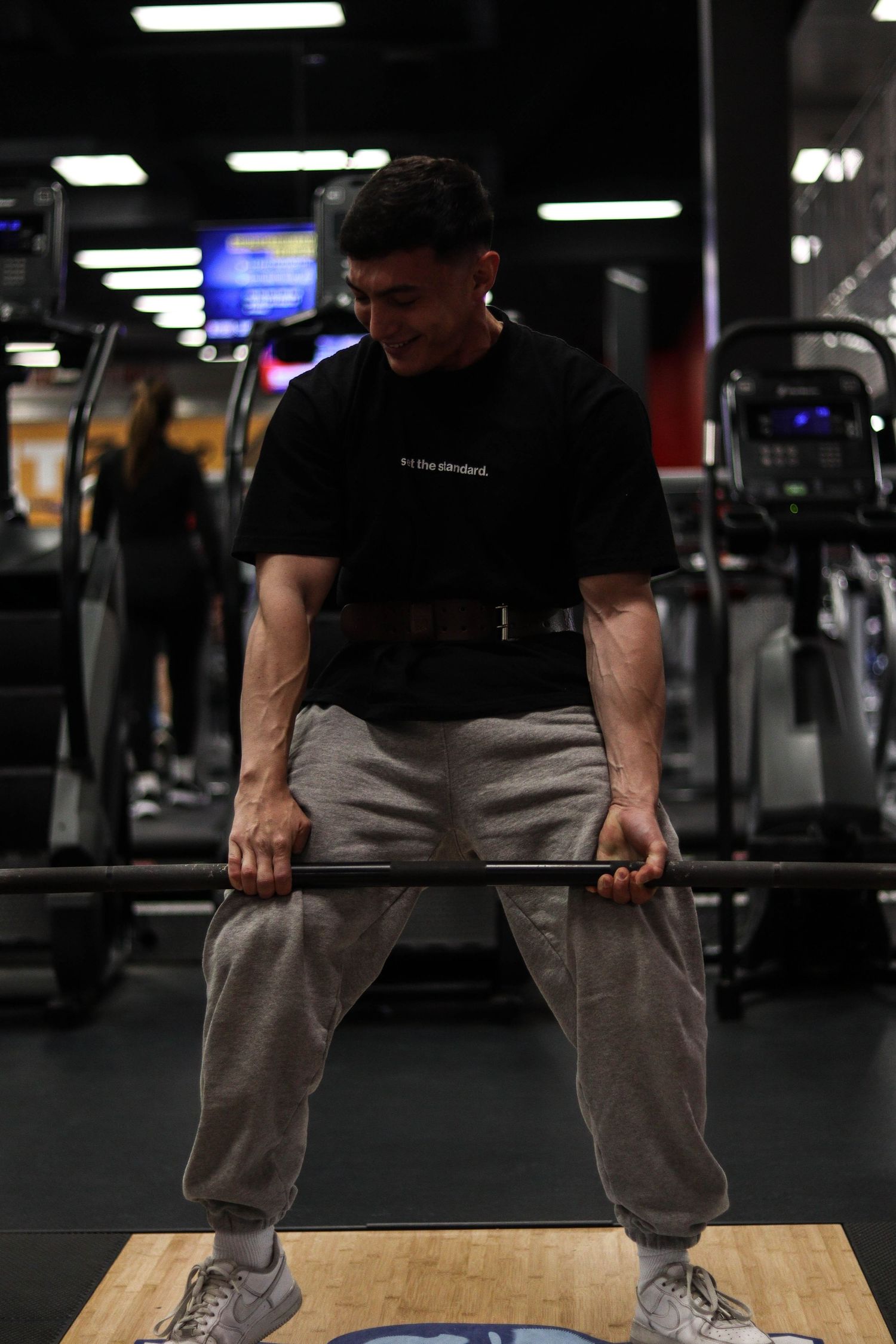Person performing deadlift exercise on a wooden platform in a dark gym setting.