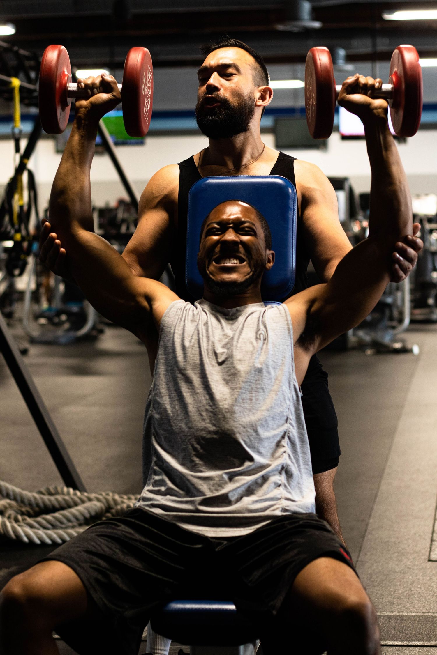 Two people working out with dumbbells at a gym, showing intense exercise form.