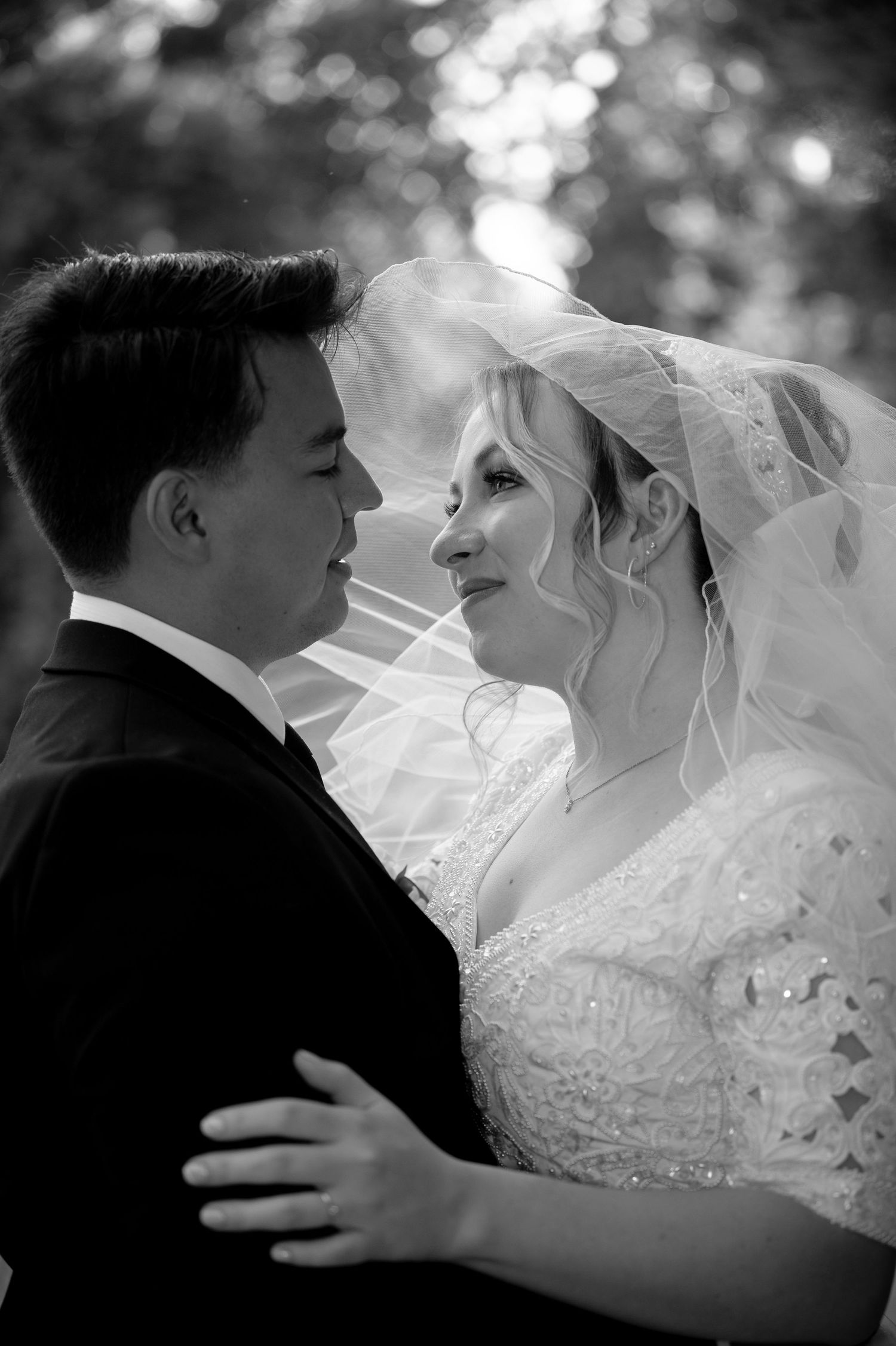 Romantic black and white wedding portrait of a bride in lace veil and groom sharing an intimate moment.