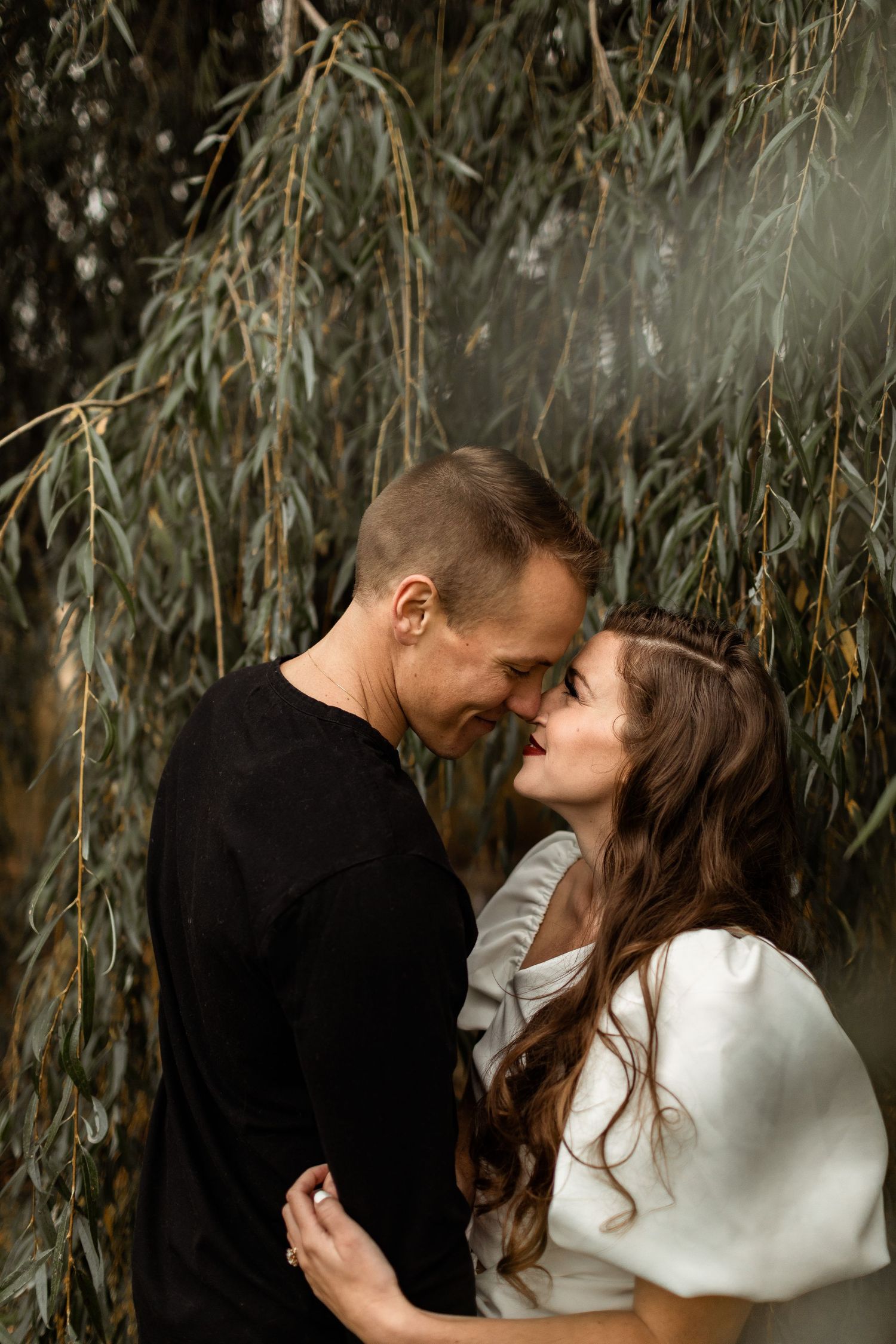Romantic couple sharing intimate moment under willow tree branches.
