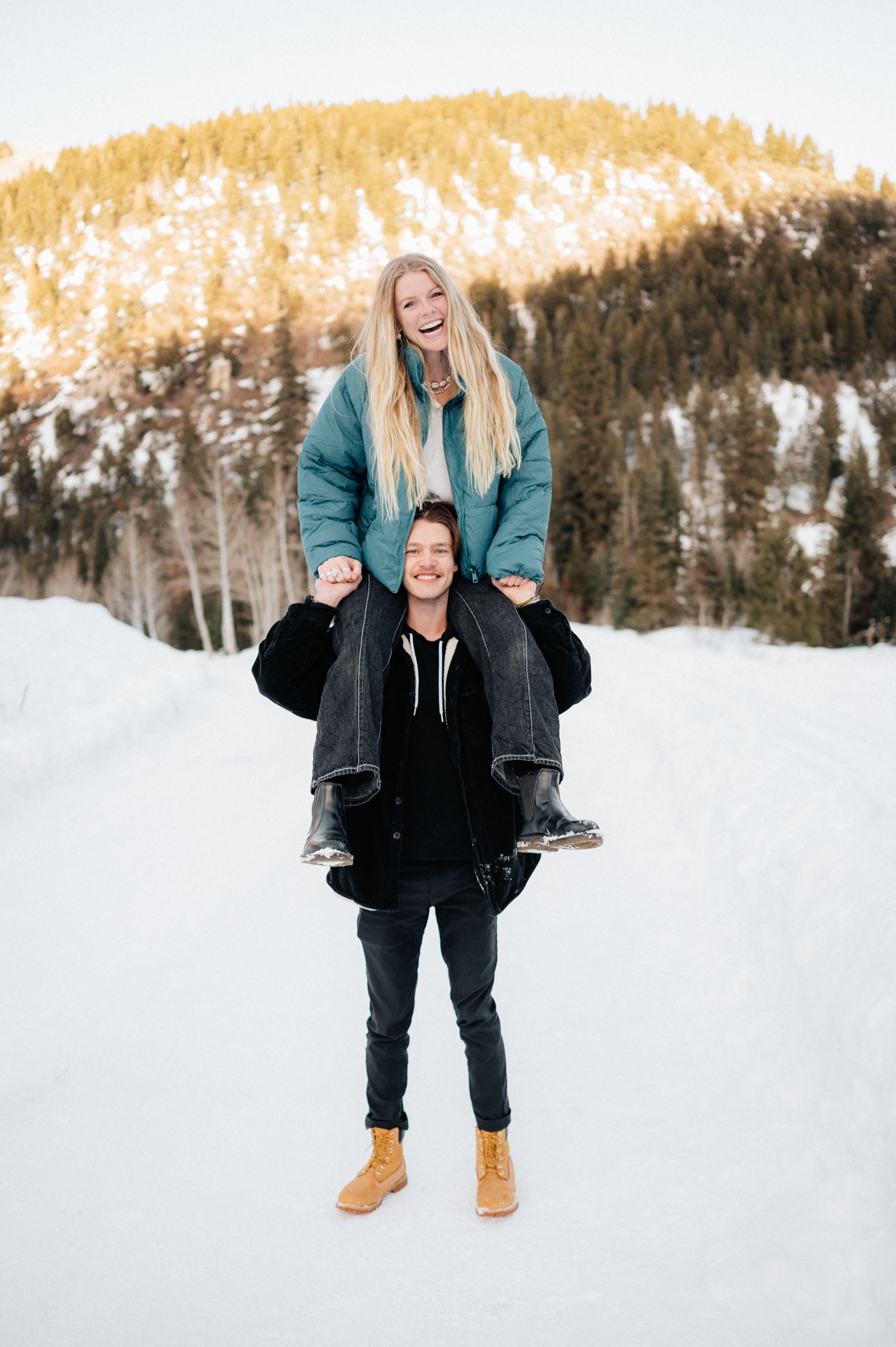 A playful winter portrait showing a couple having fun in the snow with mountains in the background.