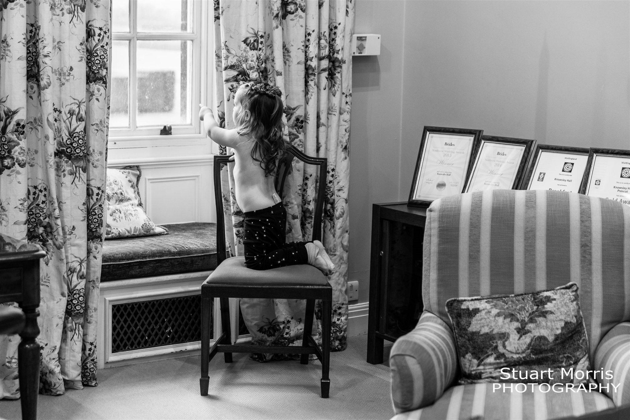 Young girl kneels on a chair to look out over the grounds at Knowsley hall. Liverpool Wedding Photographer