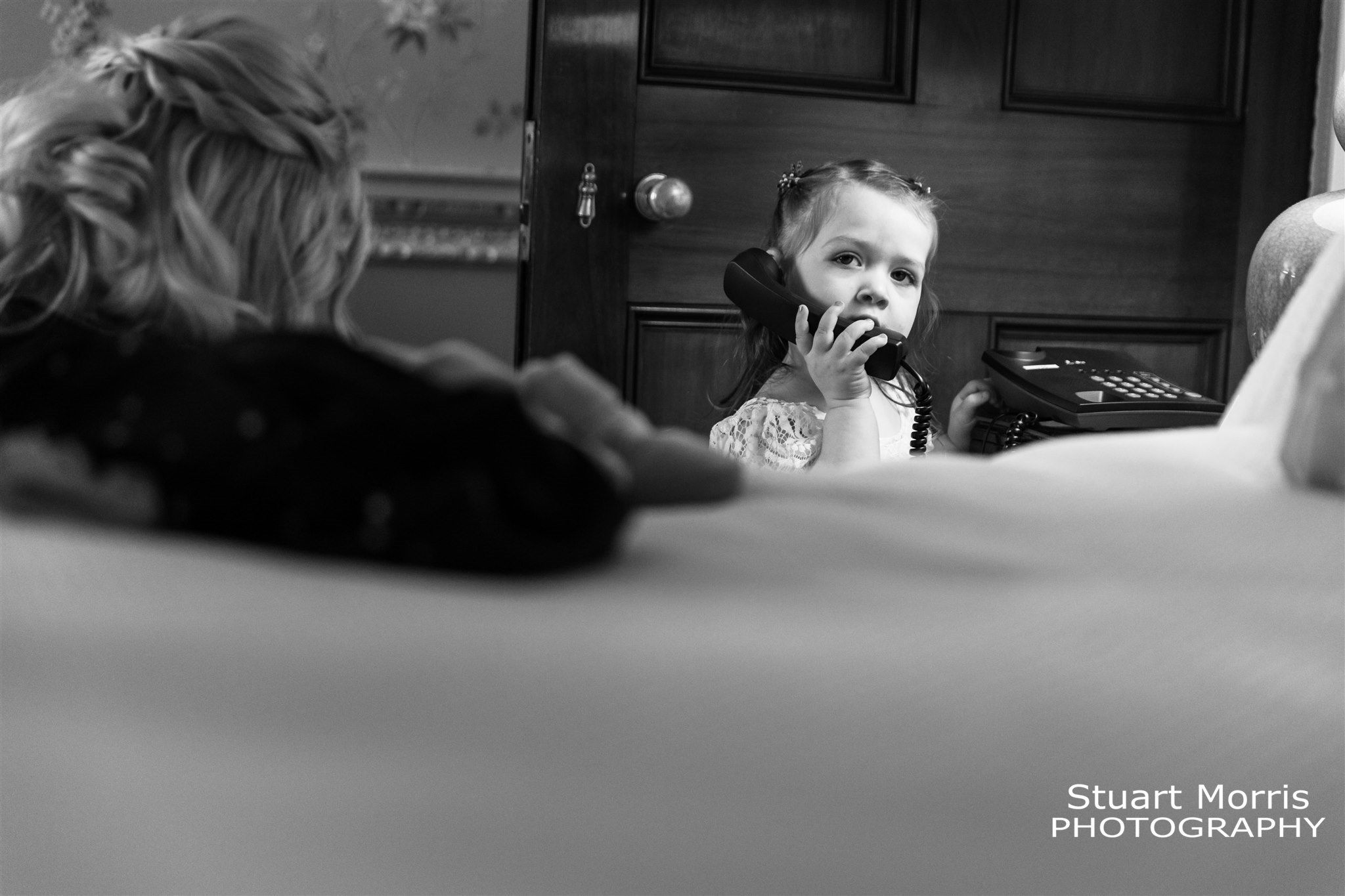 Little flower girl peeking pretends to be on the phone at the side of the bed in the dressing room Knowsley hall