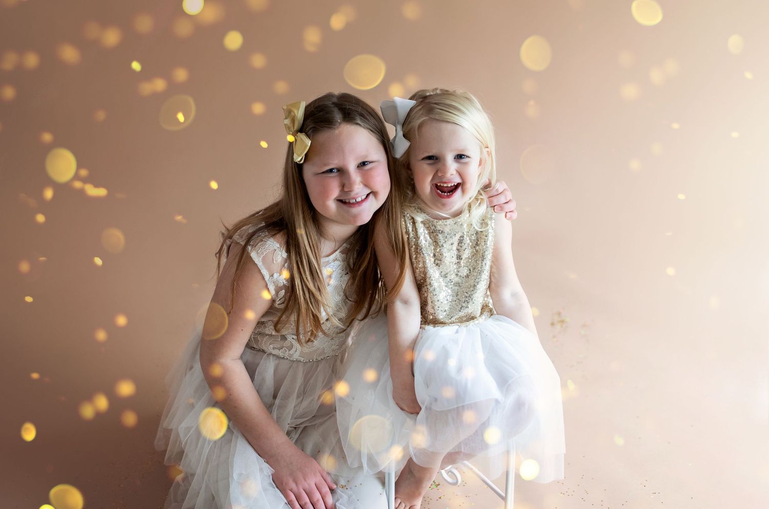 Two young girls in white dresses laughing together against a magical golden bokeh background.