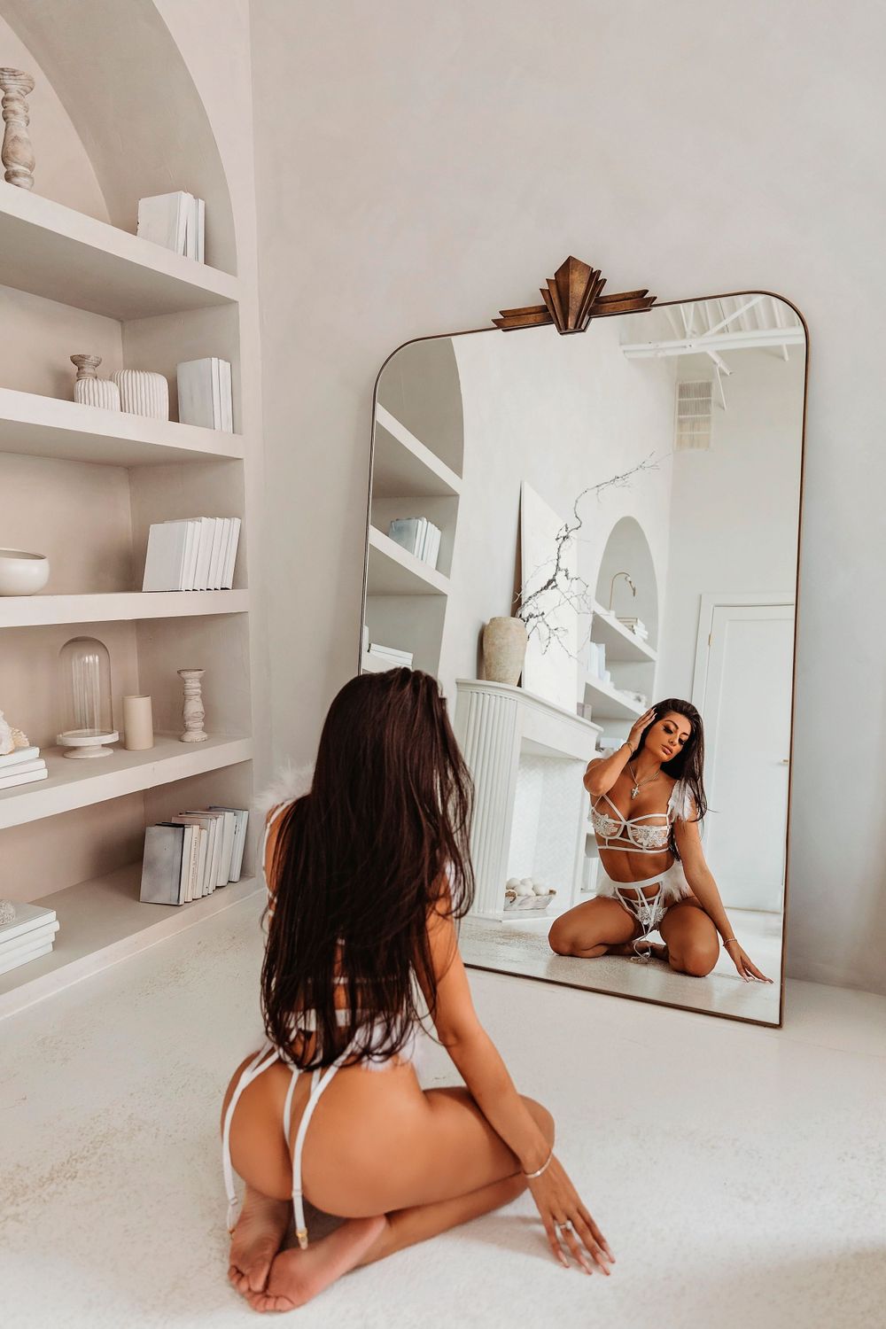 Mirror reflection in modern white interior with vintage mirror frame and built-in shelves displaying neutral decor items.